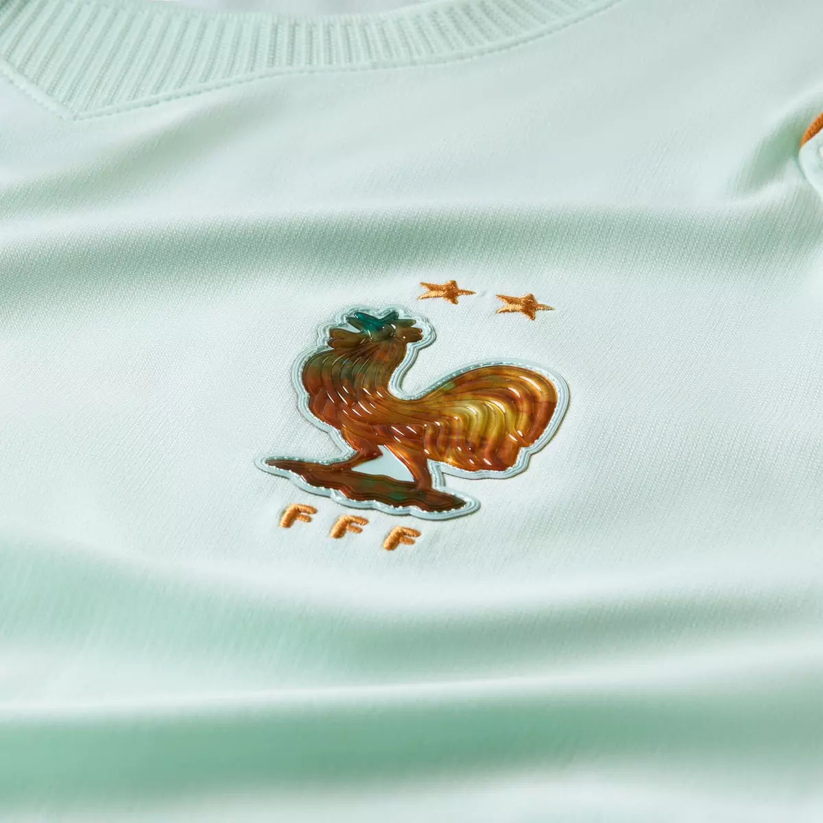 Close-up of a rooster emblem on a light green sports jersey with 'FFF' branding.