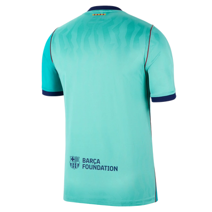 The back of a short-sleeve soccer jersey in a light turquoise/aqua color, featuring a subtle wavy pattern across the upper back, dark navy blue collar and sleeve cuffs, and the 'BARCA FOUNDATION' logo on the lower back.