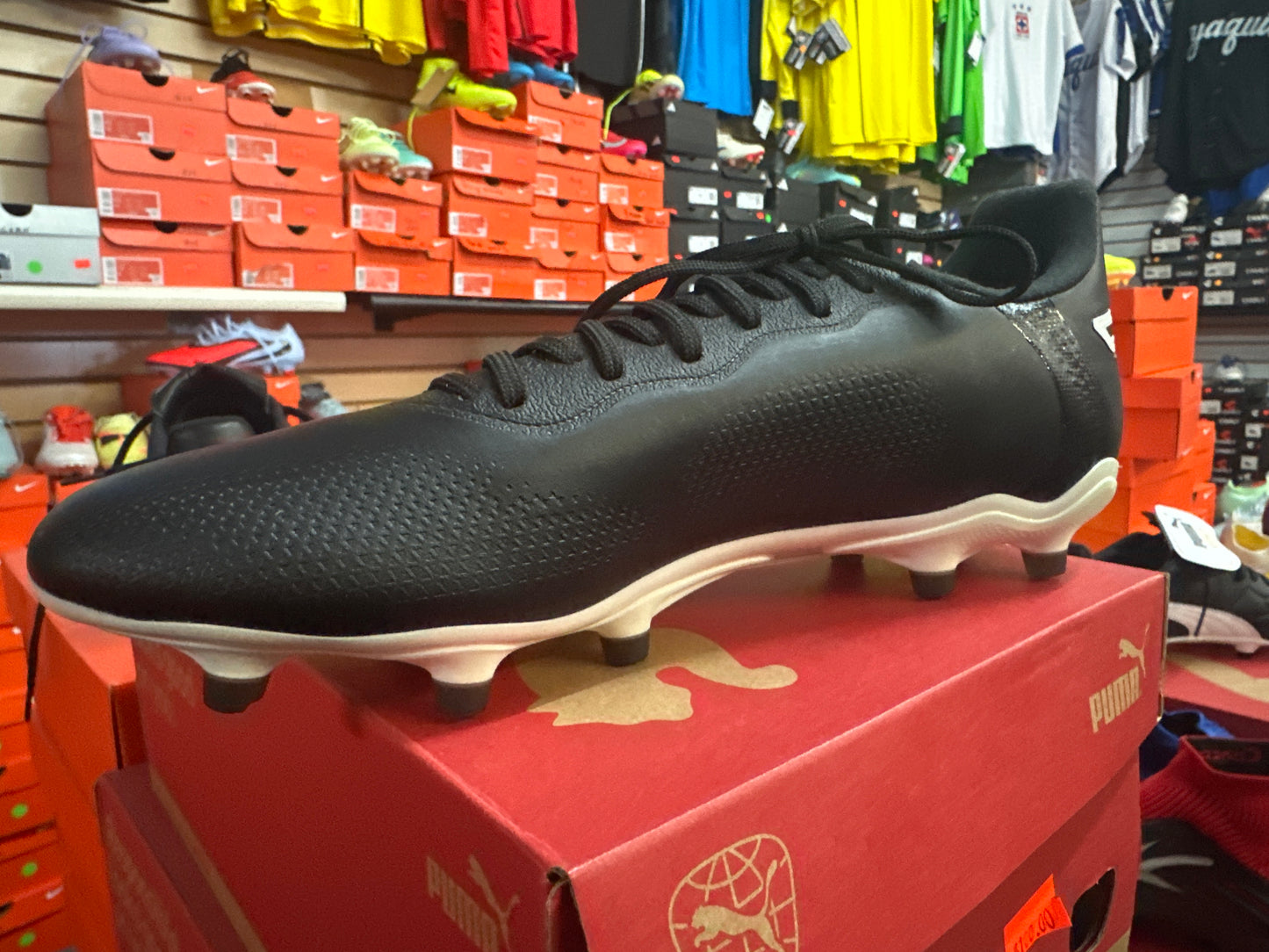 Black soccer cleat on a red Puma box with shelves of shoes and clothing in the background