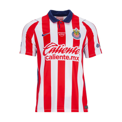 A red and white vertically striped soccer jersey with a navy blue collar, featuring the Chivas crest, a Nike swoosh, and the 'Caliente' sponsor logo on the front.